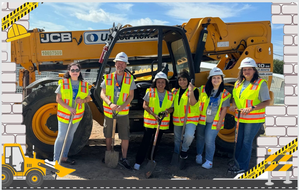 Picture of teachers in a construction site holding shovels in front of heavy-duty construction equipment.