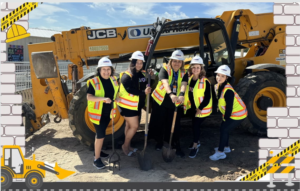 Picture of teachers in a construction site holding shovels in front of heavy-duty construction equipment.