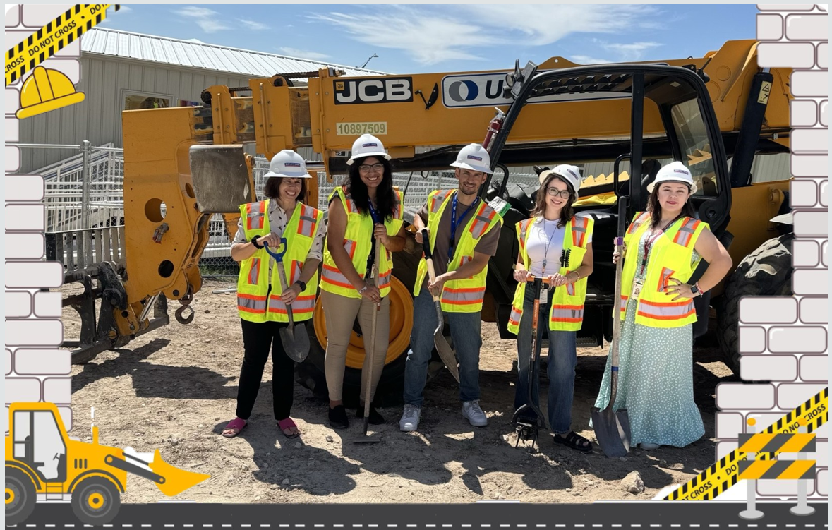 Picture of teachers in a construction site holding shovels in front of heavy-duty construction equipment.