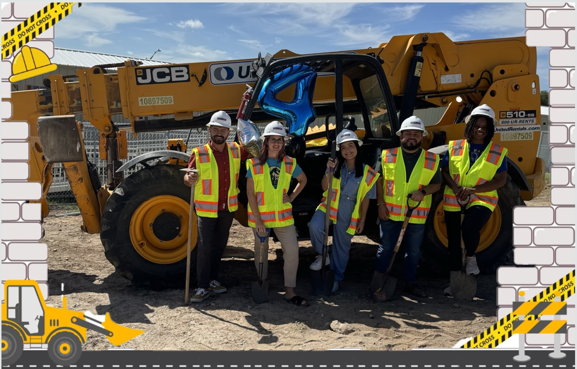 Picture of teachers in a construction site holding shovels in front of heavy-duty construction equipment.