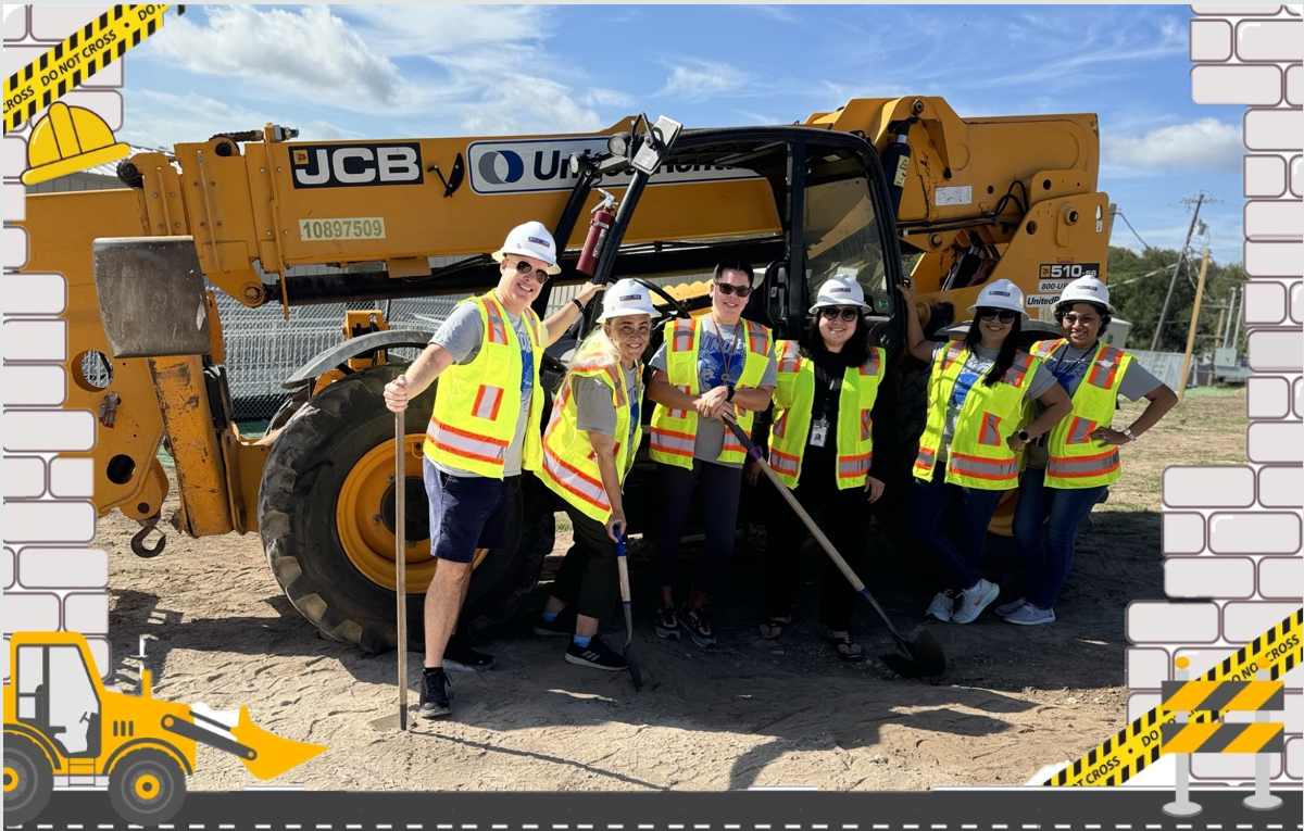 Picture of teachers in a construction site holding shovels in front of heavy-duty construction equipment.